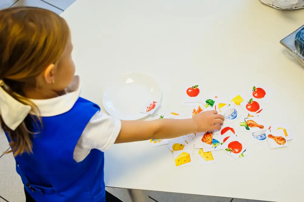 Mâna unei fetițe care așază stickere cu alimente lângă o farfurie