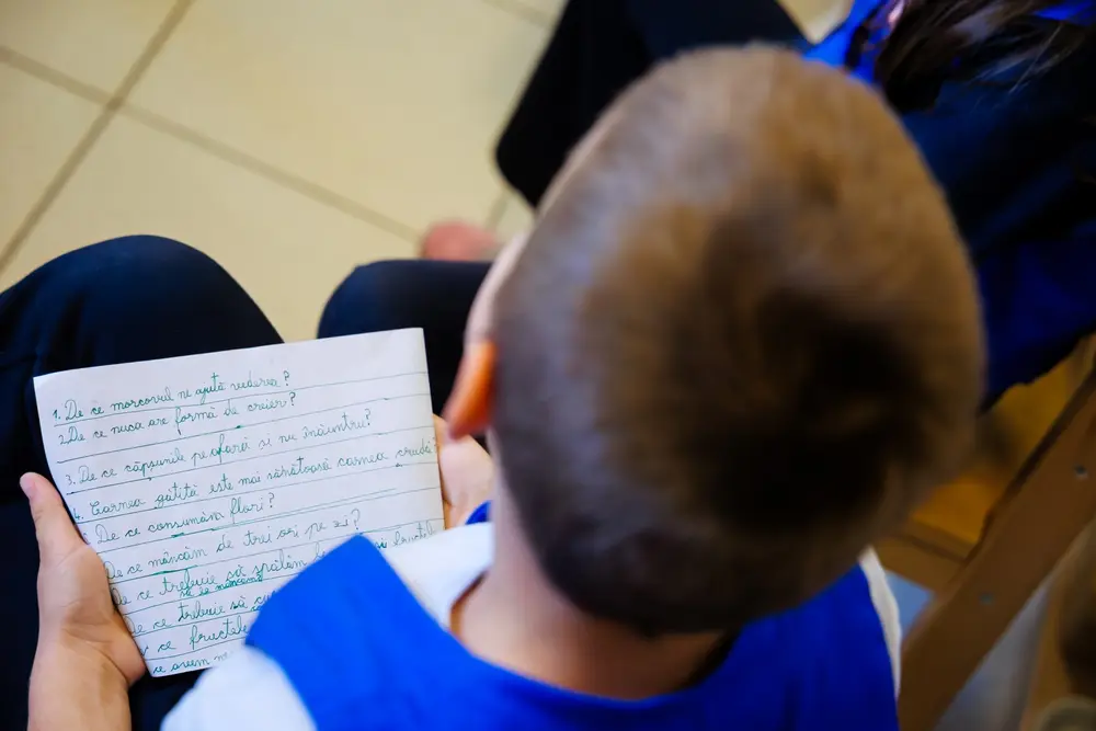 Un copil, fotografiat din spate, ține în mâini o foaie cu întrebări scrise de mână despre alimente